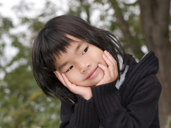 A girl has both hands on her head and smiles while outside.