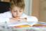 Little blonde school kid boy reading a book at home. Child interested in reading magazine for kids. Leisure for kids, building skills and education concept.